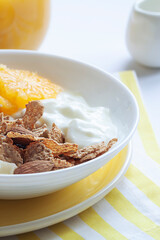Whole grain oats and wheat flakes with orange, almond nuts and yogurt in a white bowl. Healthy morning breakfast concept close up