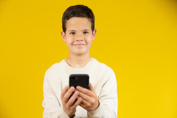 Cute boy using mobile phone isolated over yellow background.