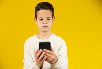 Cute boy using mobile phone isolated over yellow background.