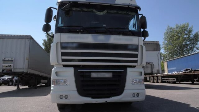 White lorry with cargo trailer drives reverse into parking place and parks with other cargo trailers.