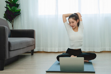 asian young woman watching video in laptop and doing home exercise in living room.