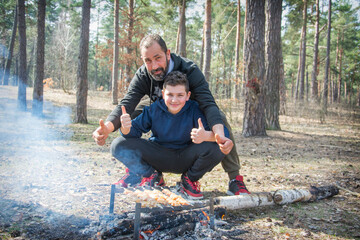 In the fall, father and son sit in the woods by the fire and grill meat.