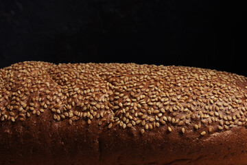 Bread crust is sprinkled with sesame seeds, light on top, black background.Dark food.