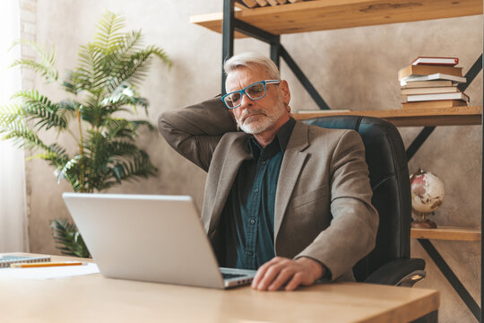 Pain in the neck. Mature man in the office at the table, migraine discomfort. Workplace stress.