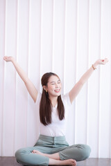Attractive beautiful Asian woman sitting on white modern room and hands up raised arms from happiness. Excited businesswoman winner success concept