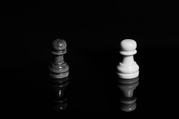 Wooden black pawn in front of white chess piece. Black isolated background with reflection. Concept of confrontation, struggle in business. Close-up, selective focus