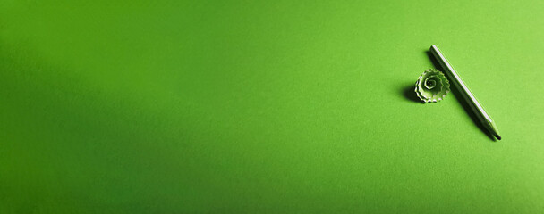 On a green light green background lies a light green pencil and pencil shavings