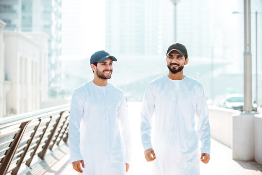 Two young men going out in Dubai. Friends wearing the kandura traditional male outfit and baseball hat in Marina