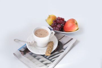closeup of cappuccino coffee in a white cup and saucer on a white background with a spoon, cookies, fruits, morning newspaper, coffee time concept, summer morning, sunny day, news