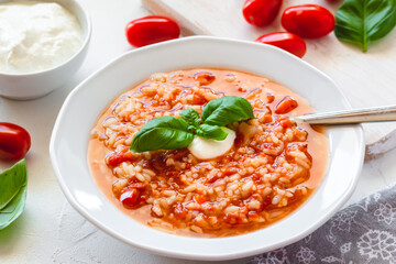 Tomato soup with rice decorated by cream and basil leaf.
