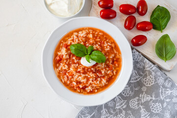 Tomato soup with rice decorated by cream and basil leaf.