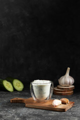 Greek tzatziki sauce in a glass glass on a rustic wooden board with cloves of garlic, cucumber in a low key