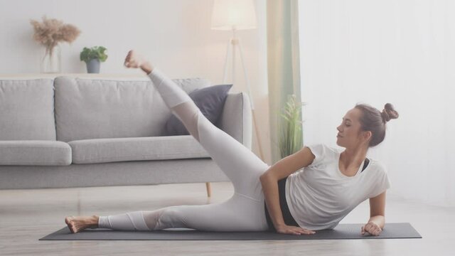 Legs strengthening exercise. Young woman working out at home, lying on floor and lifting one leg up