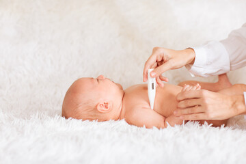 Mother's hand holding medical thermometer and measuring temperature to her baby