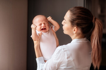 Mother with tail in white shirt holding crying newborn baby. Copy space.