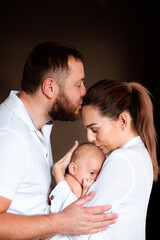 Fototapeta premium Family of three holding newborn baby, hugging and kissing each other.