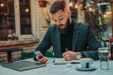 Fototapeta premium Businessman using a smartphone and a notebook in a coffee shop