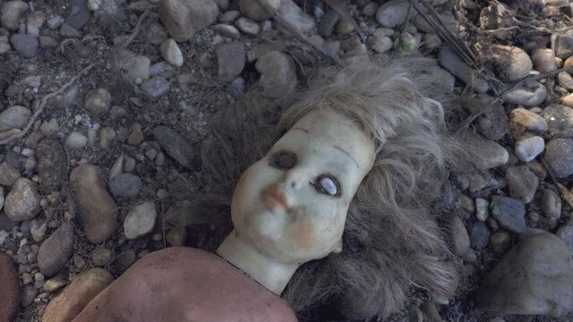 Damaged scary doll lying on river stone pebbles