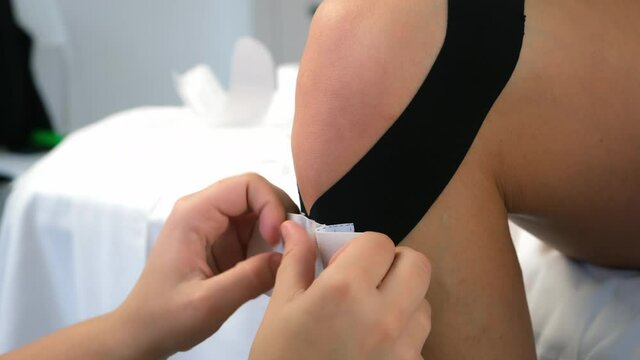 Physiotherapist chiropractor doctor applying kinesiology tapes to woman's leg to fix the knee joint. Use of tapes in medicine for fixation of muscles, joints. Recovery rehabilitation after an injury.