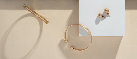 Panoramic shot of golden bracelets and earrings on white box on beige background
