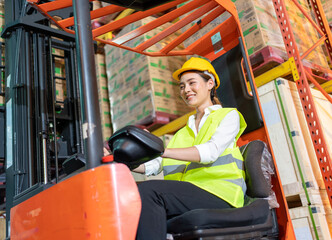 Forklift driver asian young woman in safety jumpsuit uniform with yellow hardhat at warehouse. Worker female  working and smiling in forklift loader work © BigBlues