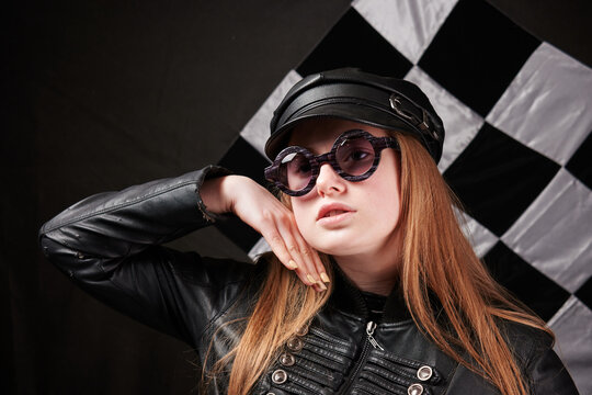 portrait of young girl in leather cap and glasses. checkered black and white background