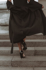 Woman in black coat and high heels shoes walking up the steps. Back view