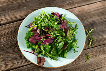 salad mix of fresh herbs, arugula, Swiss chard, spinach in tarenle on a wooden background, top-side view