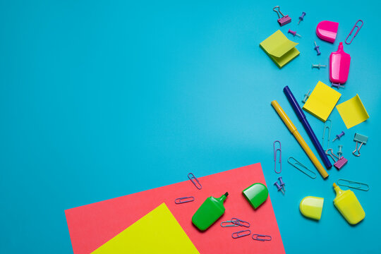 Stationery items on the blue background with free space for text. Creative, colorful background with scool or office supplies. Flatlay with copy space, top view. Markers, paper clips, sticky notes.