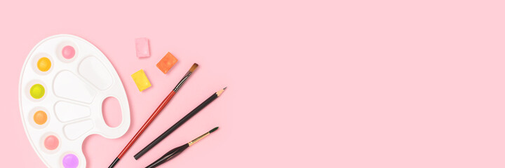 Banner with watercolor palette and paintbrushes on a pink background. Artistic concept with copyspace.