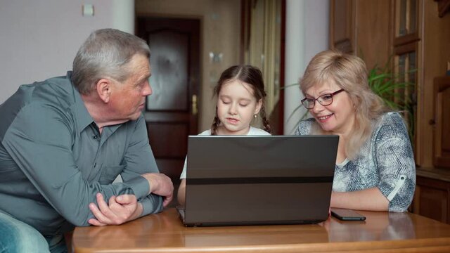 Smiling young little grown granddaughter teaching old grandparents using laptop notebook at home indoors. Talking people in medium shot. Smiling 2 two generations