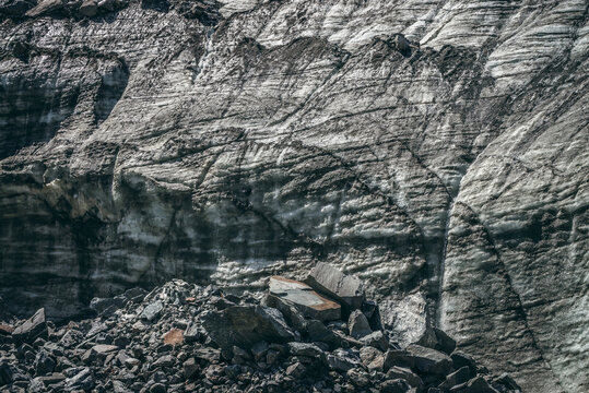 Nature background with icefall near glacier with cracks and scratches. Natural backdrop with icy wall and moraines. Beautiful landscape with shiny glacial wall and stones in sunlight. Glacier texture.