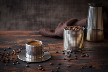 Steel cup of coffee, blended coffee beans in a tin can and geyzer coffee maker, brown napkin on a...