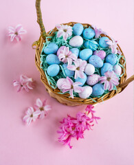 Wicker basket with chocolat eggs and spring bright flowers, selective focus