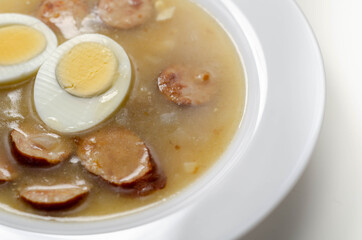 Traditional polish sour soup with sausage and eggs in a white deep plate