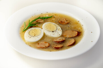 Traditional polish sour soup with sausage and eggs in a white deep plate