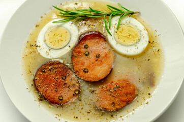 Traditional polish sour soup with sausage and eggs in a white deep plate