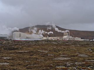 Fototapeta na wymiar View of steaming Svartsengi geothermal power station near Grindavik, Reykjanes peninsula, Iceland with moss covered lava field in front on cloudy winter day.