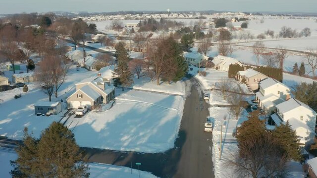 Aerial tracking shot through neighborhood housing development. Winter snow on sunny day in Pennsylvania, USA.