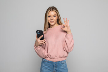 Fototapeta premium Attractive woman showing ok gesture while holding blank screen mobile phone over gray background