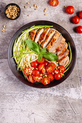 Fried chicken fillet and fresh vegetable salad of tomatoes, zucchini and pine nuts.