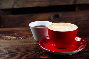 Coffee in a red cup with milk and latte art and coffee in a white cup on a table