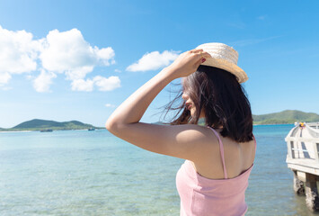 Near of asian woman tan skin wearing pink tank top and hold straw hat. She looking into the sea. Summer travel. Relaxing, Holiday and tropical relax concept.