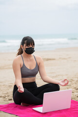 Young woman meditating with a laptop at the beach