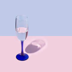 Blue champagne glass with alcohol liquid against bright pastel blue and pink color backdrop. Celebration minimal style New Year party background.