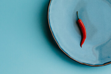Red pepper on a blue plate and color background.