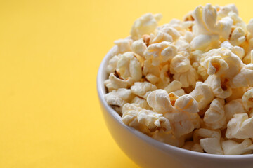 Popcorn in a white bowl on yellow colored background. Top view, copy space