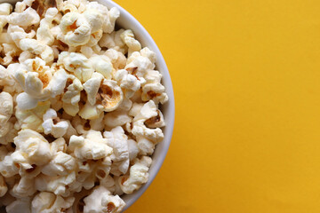 Popcorn in a white bowl on yellow colored background. Top view, copy space