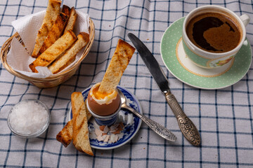 breakfast with a soft-boiled egg on a stand, croutons and a cup of coffee