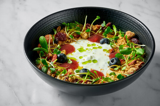 Healthy breakfast bowl of granola with dried fruits, berries, nuts, microgrin and yogurt on a light marble background